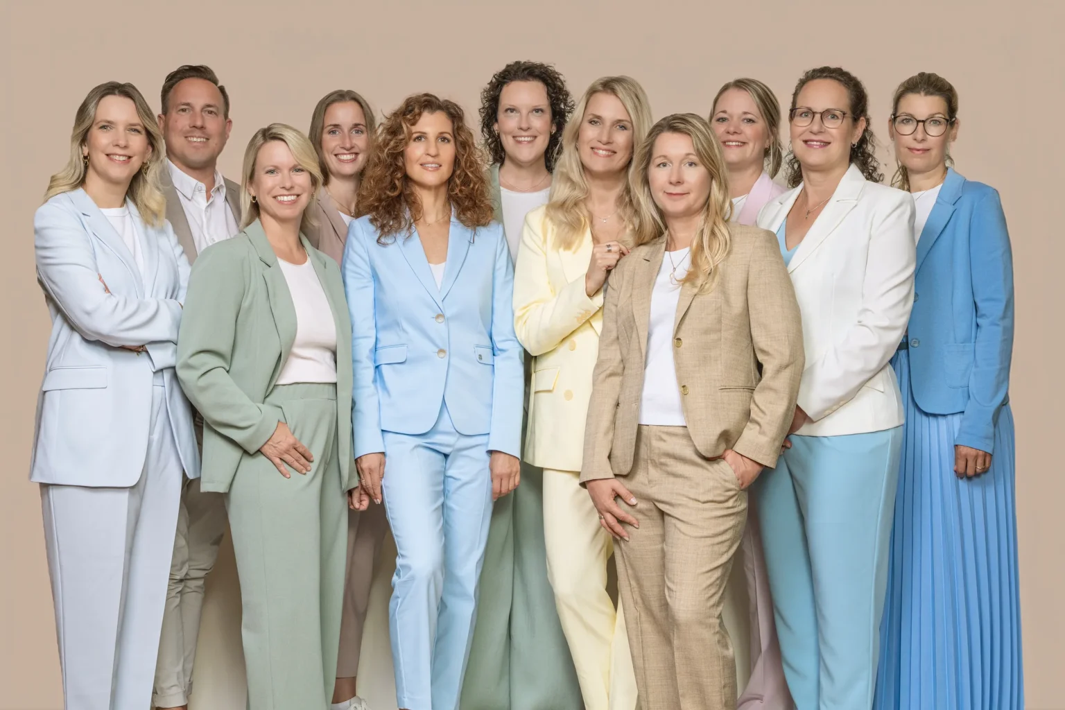 Das Team von Die Hotelspezialisten: elf Partnerinnen, Partner und Projektmitarbeiterinnen in hellen Anzügen vor beigem Hintergrund